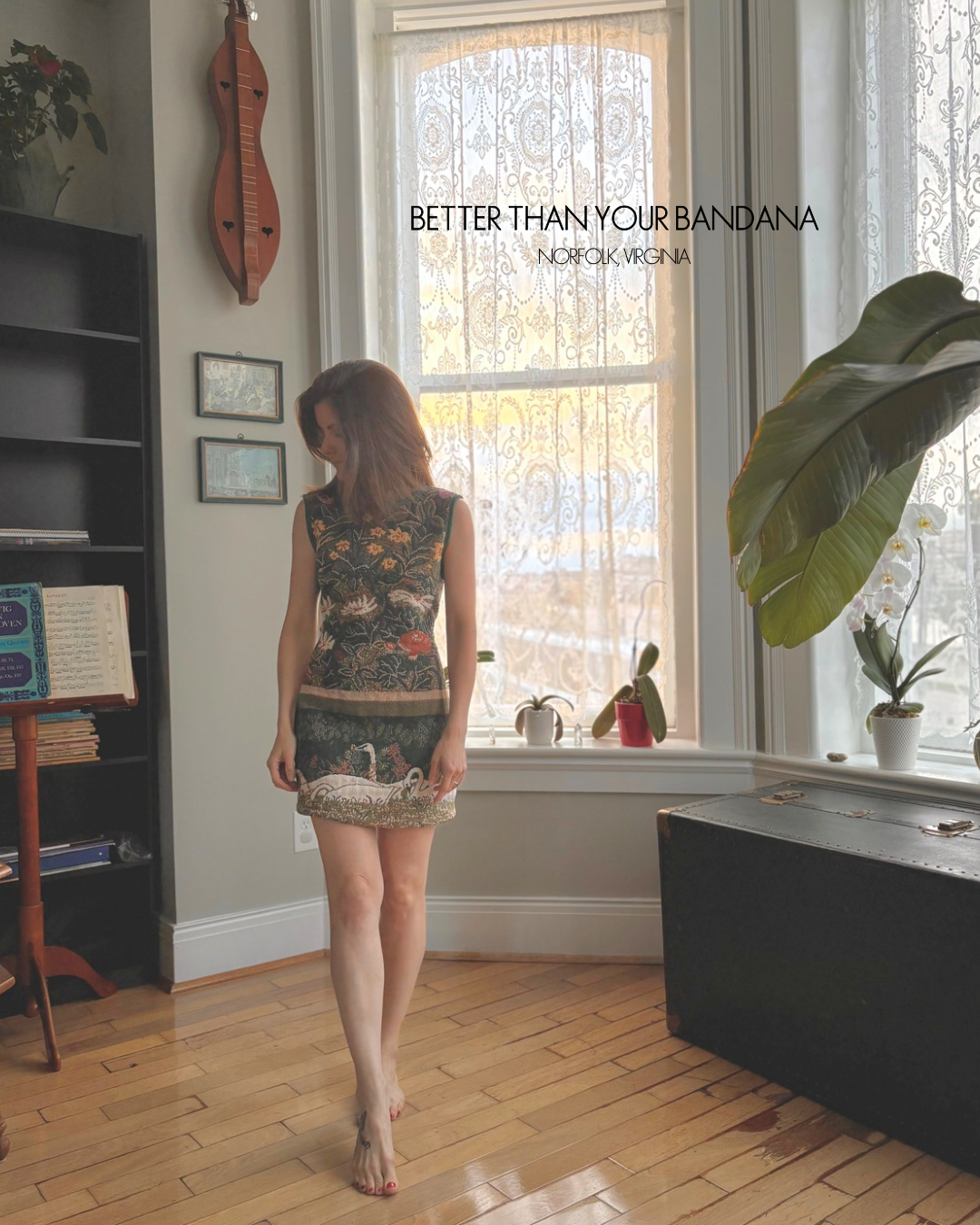 A woman stands barefoot in a room with hardwood floors and a large window, wearing a sleeveless patterned mini dress. Text on the image reads 'BETTER THAN YOUR BANDANA NORFOLK, VIRGINIA.